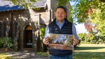 Vicar Tim Stevens at Guyra Anglican Church holding his compeition winning picture of the church in Autumn. Picture supplied.