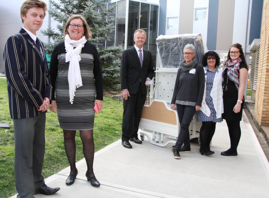 TAS Senior Prefect Ben Moffatt presents one of two palliative care beds to Hunter New England Health Oncology social worker Fiona Ord, watched by TAS Headmaster Murray Guest, clinical nurse specialists Kim Taylor and Angie Newton, and UNE social work Masters student Olivia Monk.